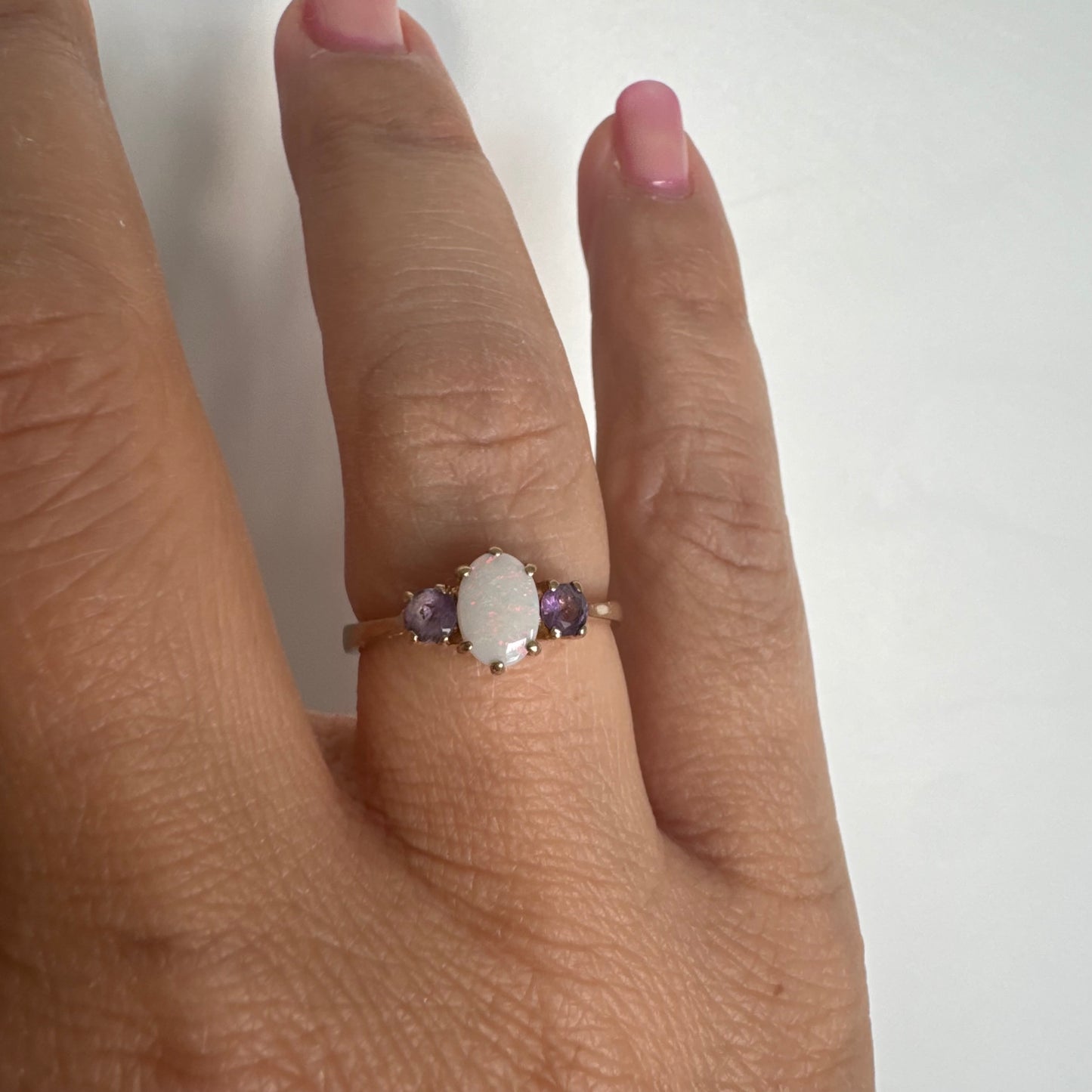 9K gold ring set with an oval Opal at the center, flanked by two delicate purple stones.