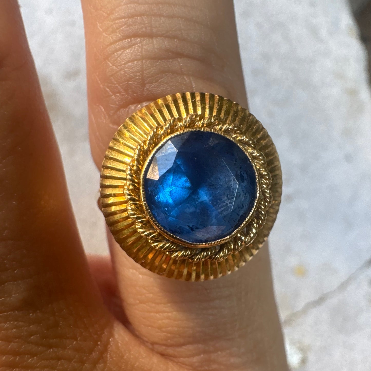 18K gold ring featuring a vibrant round Blue Topaz set in a textured gold bezel.