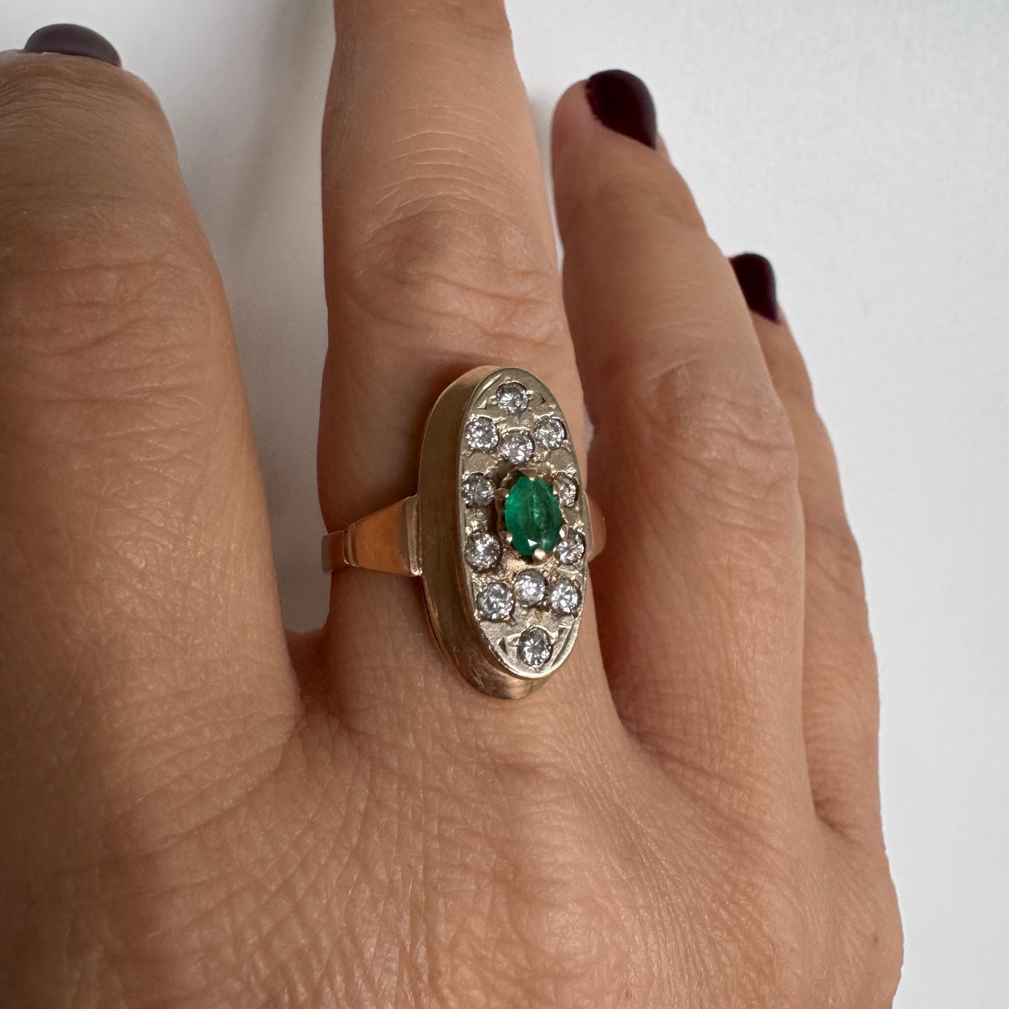 טבעת זהב 14 קראט בעיצוב אלגנטי ומאורך, משובצת אבן אמרלד מרכזית ויהלומים מסביב.