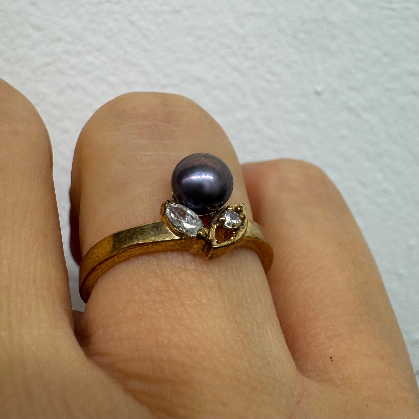 14K gold ring set with a Black Pearl at the center and clear gemstones on the sides.