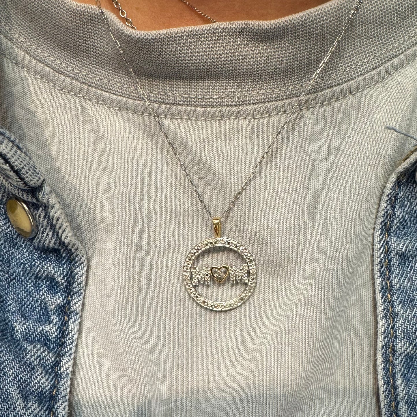 תליון זהב לבן 14 קראט עם הכיתוב ״MOM” מוקף מסגרת יהלומים עדינה.