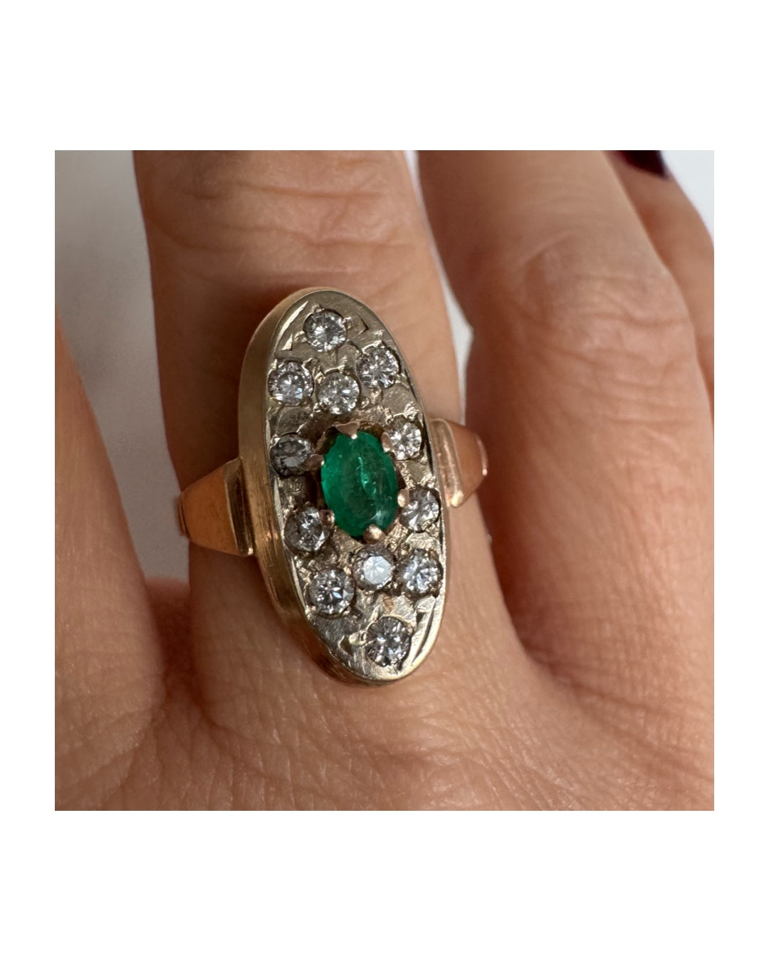 טבעת זהב 14 קראט בעיצוב אלגנטי ומאורך, משובצת אבן אמרלד מרכזית ויהלומים מסביב.