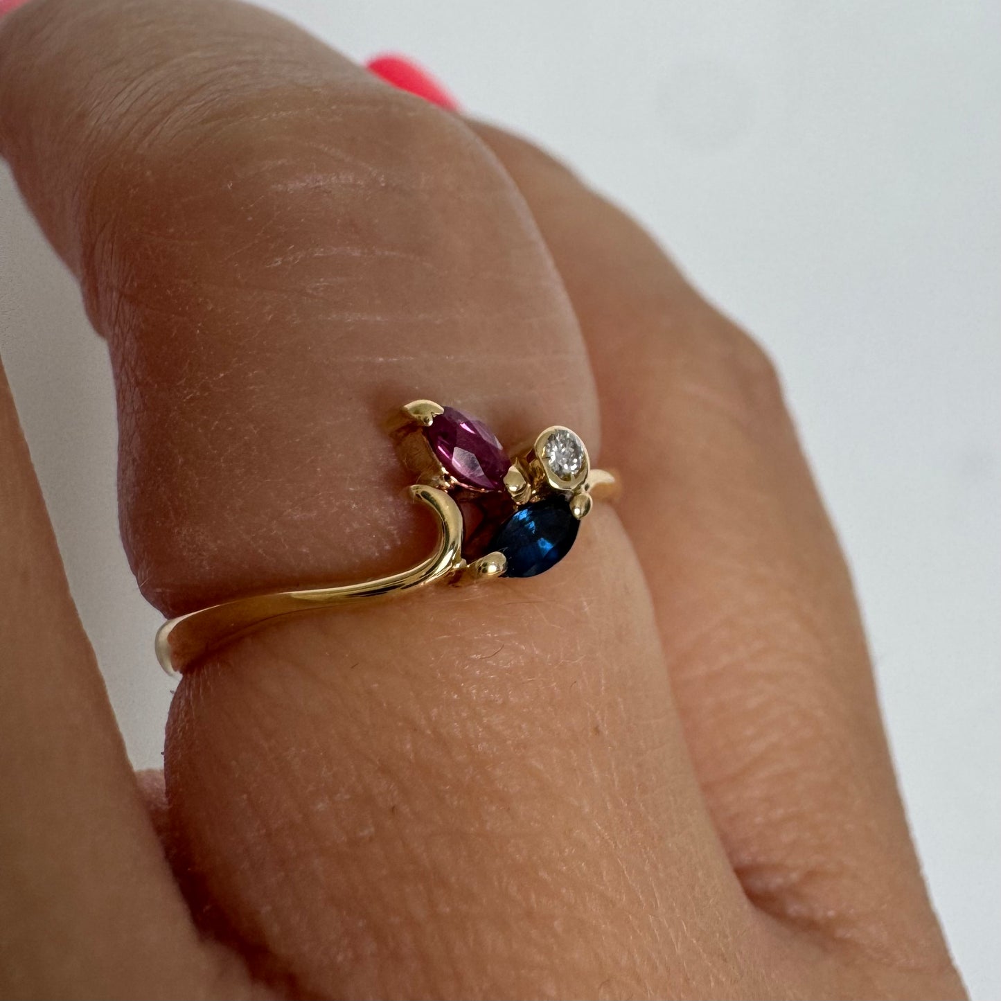 Delicate 18K gold ring set with pink and blue Sapphires alongside a sparkling center stone.