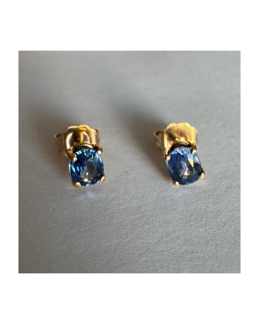 עגילי זהב 14 קראט קטנים צמודים לאוזן משובצים אבני טנזנייט בחיתוך אובלי, בגוון כחול־סגלגל עמוק ומעודן.