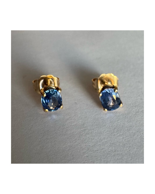 עגילי זהב 14 קראט קטנים צמודים לאוזן משובצים אבני טנזנייט בחיתוך אובלי, בגוון כחול־סגלגל עמוק ומעודן.