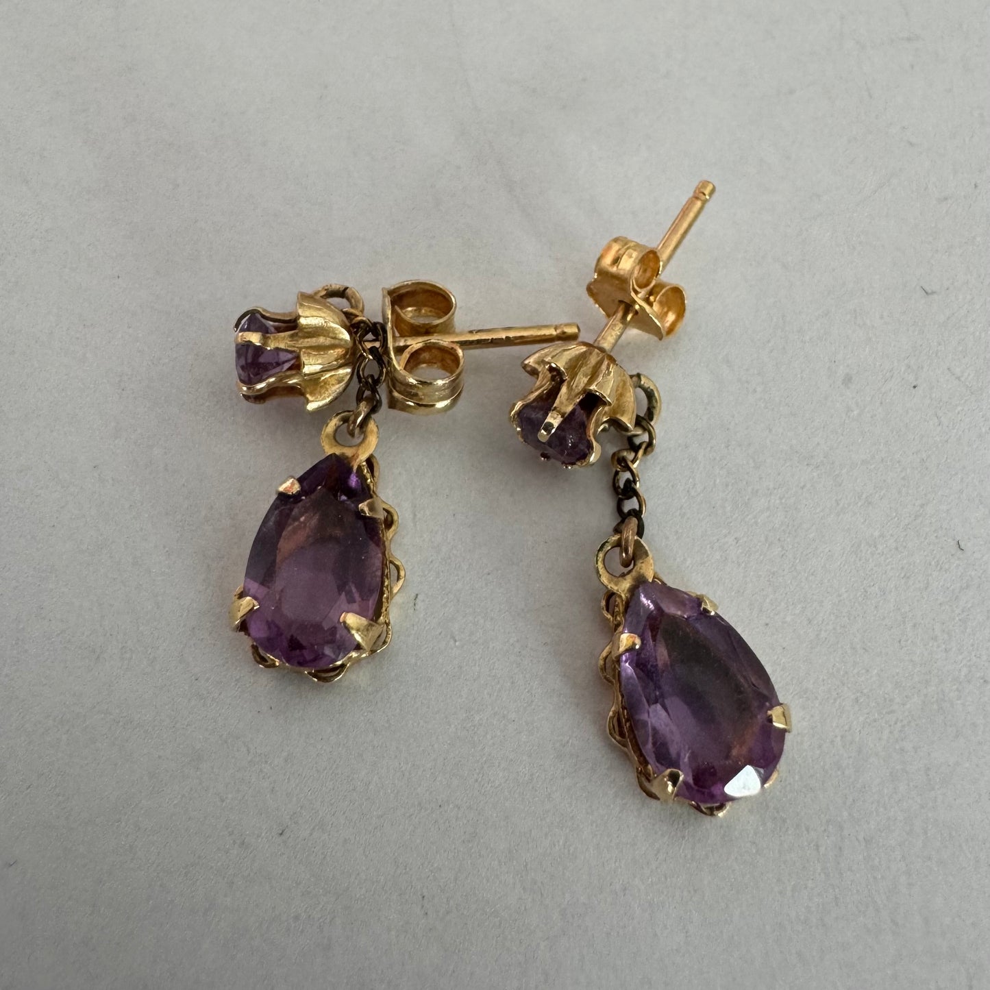 עגילים זהב צהוב 14 קראט משובצים אבני אמטיסט בגוון סגול עמוק בחיתוך טיפה, בשילוב אבן עליונה תואמת ועיטור שרשרת עדינה המחברת ביניהן.