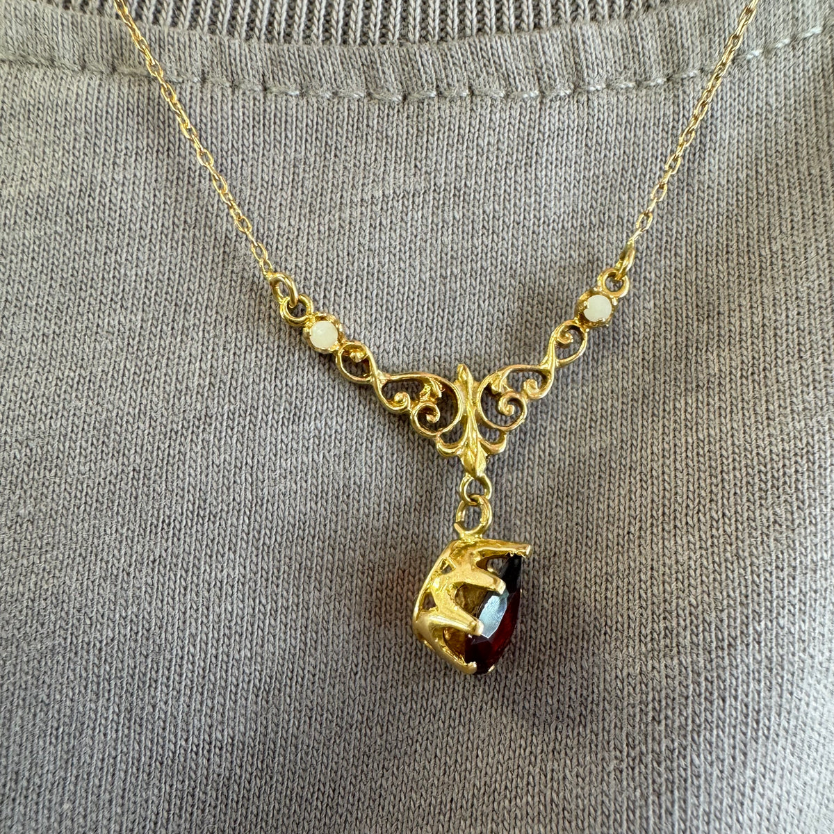 18K gold Necklace featuring an elegant scrollwork design and a striking deep-red pear-shaped Garnet drop.