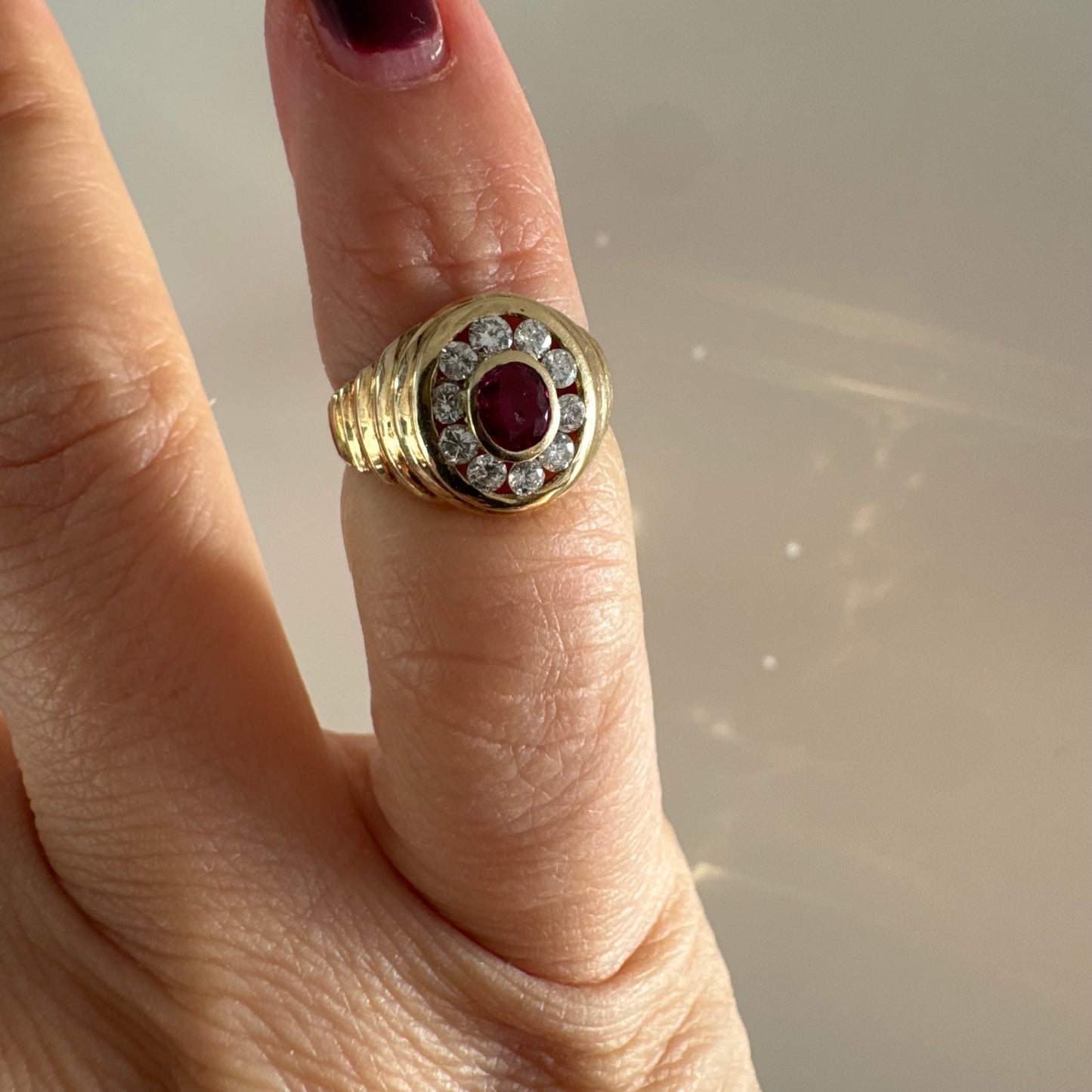 טבעת זהב צהוב 14 קראט בסגנון חותם עגול, משובצת אבן רובי מרכזית וסביבה הילה של יהלומים עגולים.