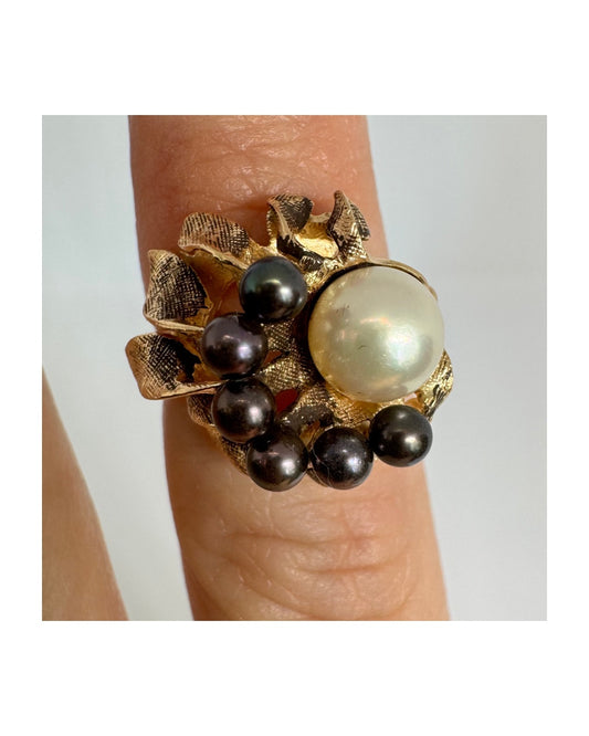 14K gold ring set with a luminous white Pearl at its center surrounded by a delicate circle of black Pearls.