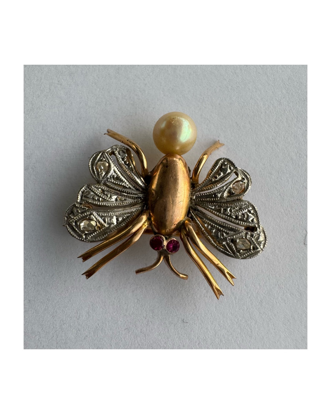 סיכת חרק ייחודית עשויה זהב 14 קראט משובצת יהלומים בעבודת פיליגרן עדינה בכנפיים, אבני רובי אדומות בעיניים ופנינה טבעית בגוון שמפניה.