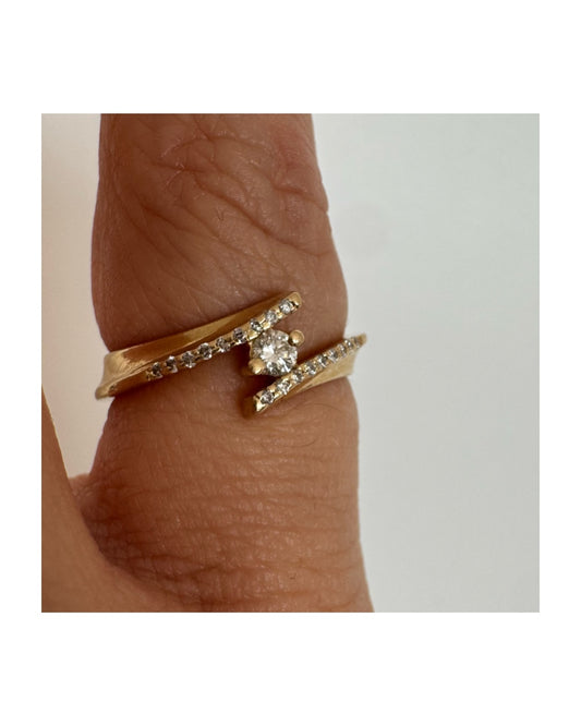 טבעת זהב 14 קראט בעיצוב פתוח ואלגנטי, משובצת יהלום מרכזי ויהלומים עדינים לאורך הזרועות.