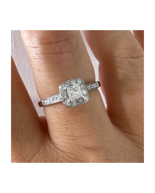 טבעת זהב לבן 14 קראט משובצת יהלום מרכזי בחיתוך פרינסס, מוקף הילת יהלומים קטנים וזרוע משובצת פאווה